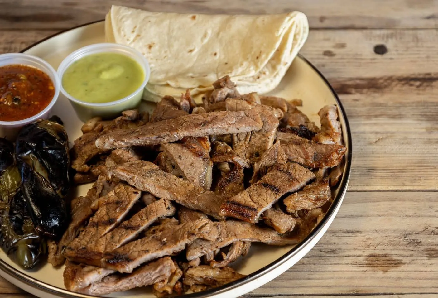 Carne asada en tiras con tortillas, salsa roja, salsa verde y chiles toreados