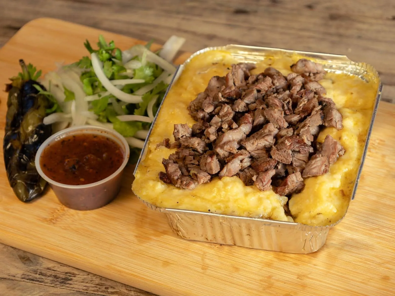 Charola de carne asada picada sobre puré gratinado, con salsa, chile toreado y cebolla con cilantro