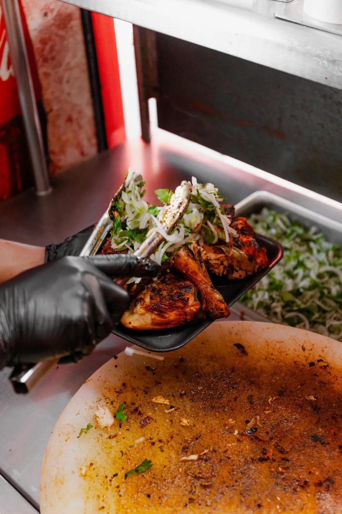 Parrillero con guantes sirviendo pollo asado con cebolla y cilantro frescos