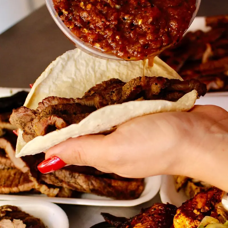 Taco de carne asada en tortilla de harina mientras le sirven salsa roja