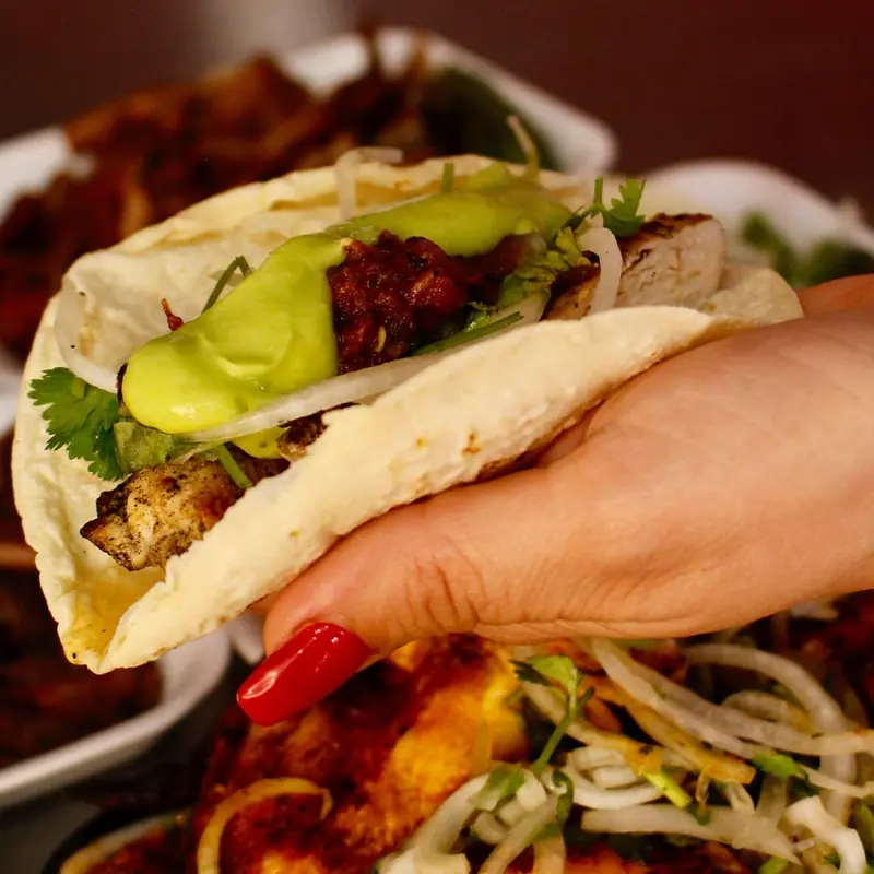 Taco de pollo con salsa roja, cebolla, cilantro y salsa verde cremosa